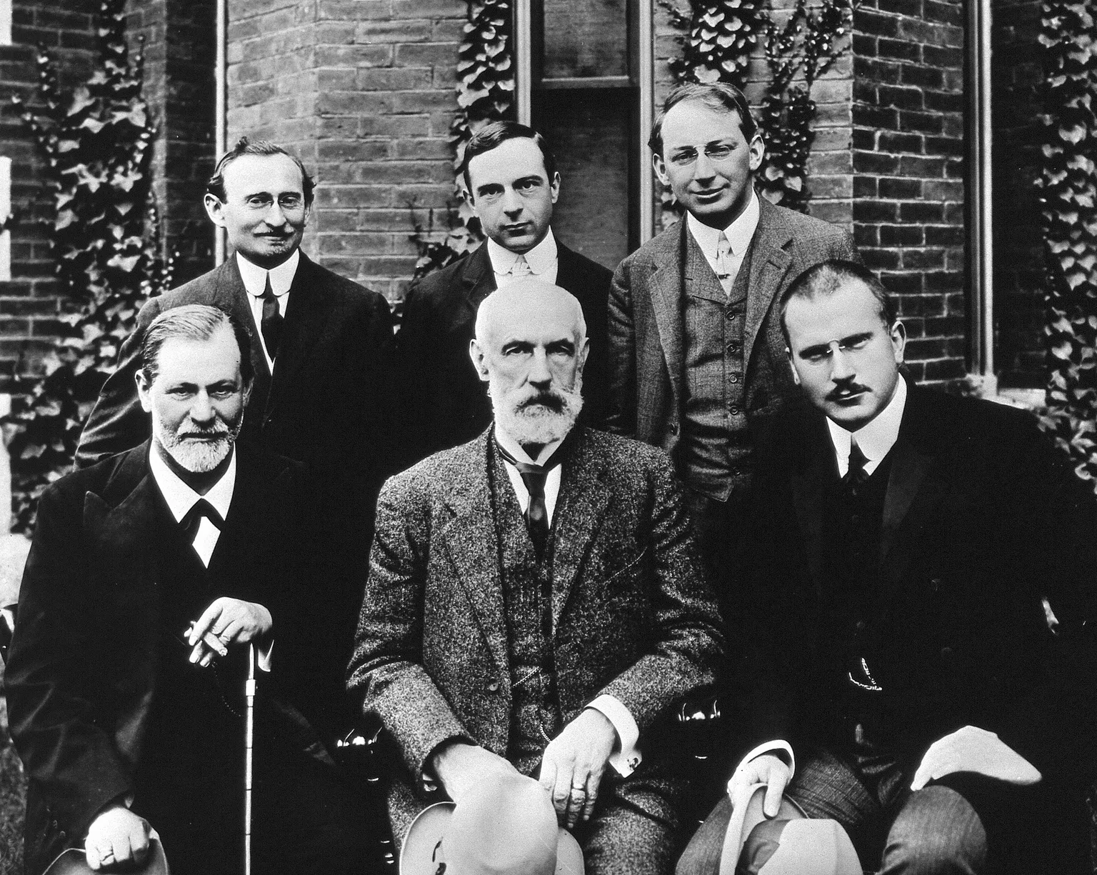 Six men posed in front of an ivy-covered brick building at Clark University in 1909. Seated in front: Sigmund Freud, G. Stanley Hall, and Carl Jung. Standing behind them: Abraham Brill, Ernest Jones, and Sandor Ferenczi.